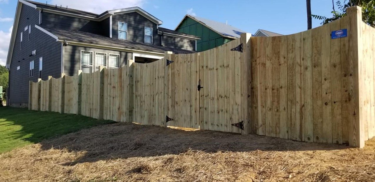 Wooden privacy fence along a grassy yard beside a house on a sunny day