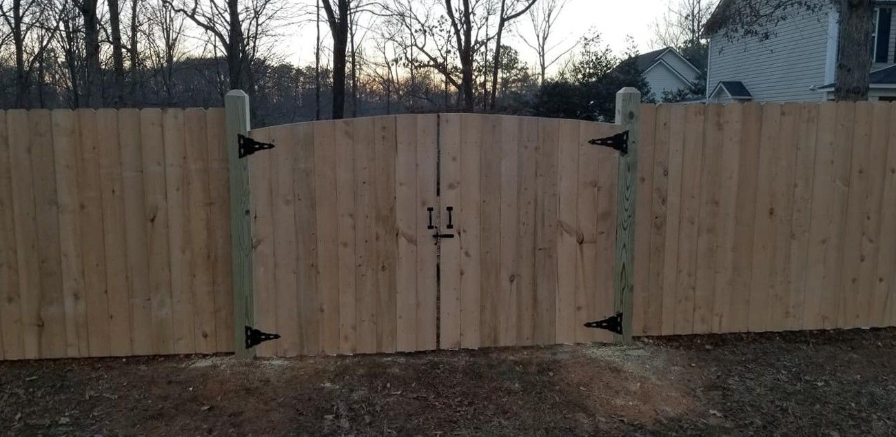 Wooden driveway gate closed across a fenced entrance at dusk.