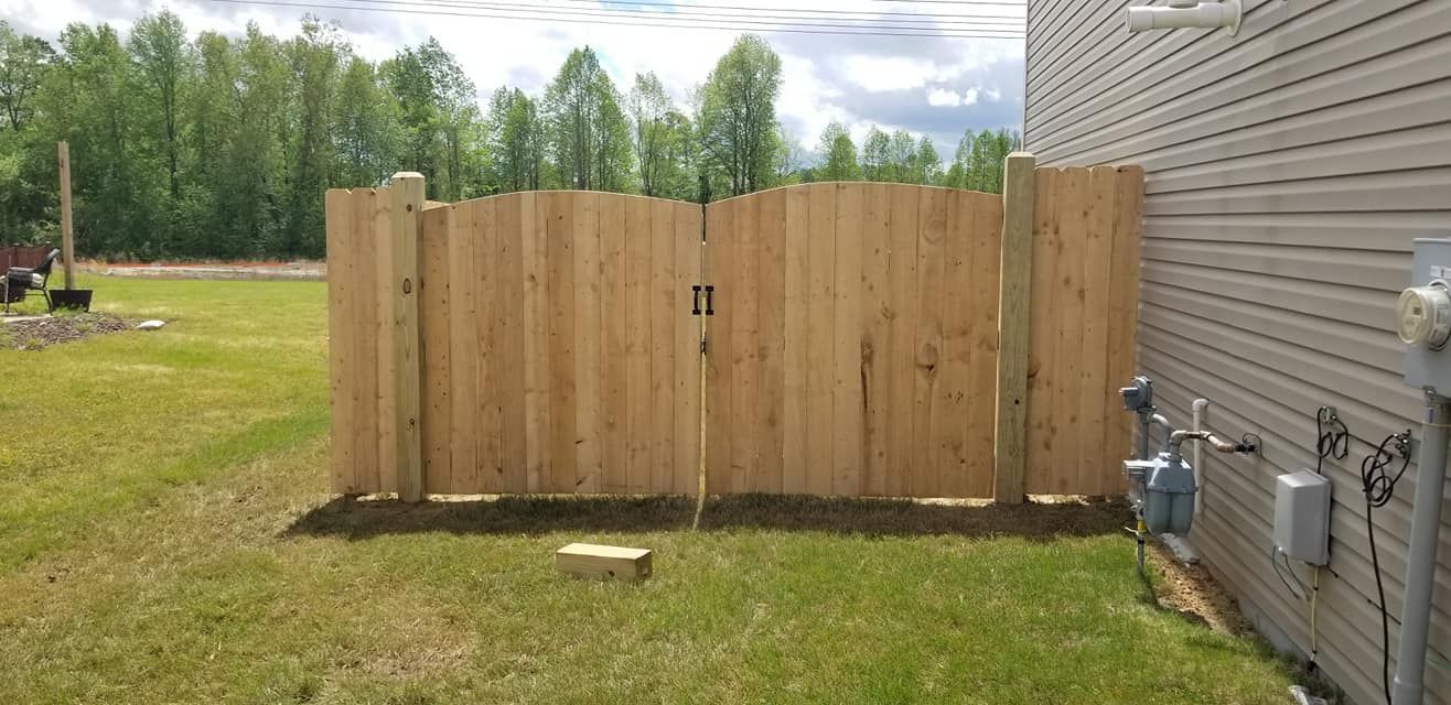 Wooden privacy fence beside a house in a grassy yard, with trees and cloudy sky in the background
