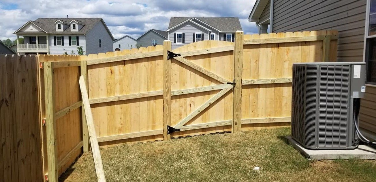 Wooden backyard fence with open gate beside a house and HVAC unit under a cloudy sky