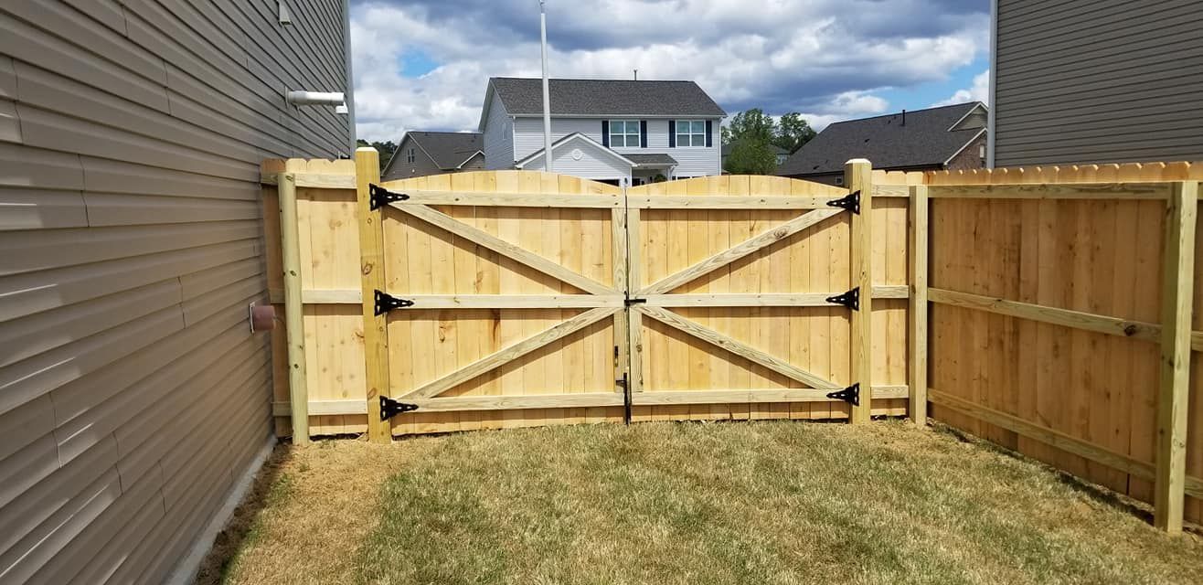 Backyard with a wooden fence, open gate, and grassy lawn beside a house
