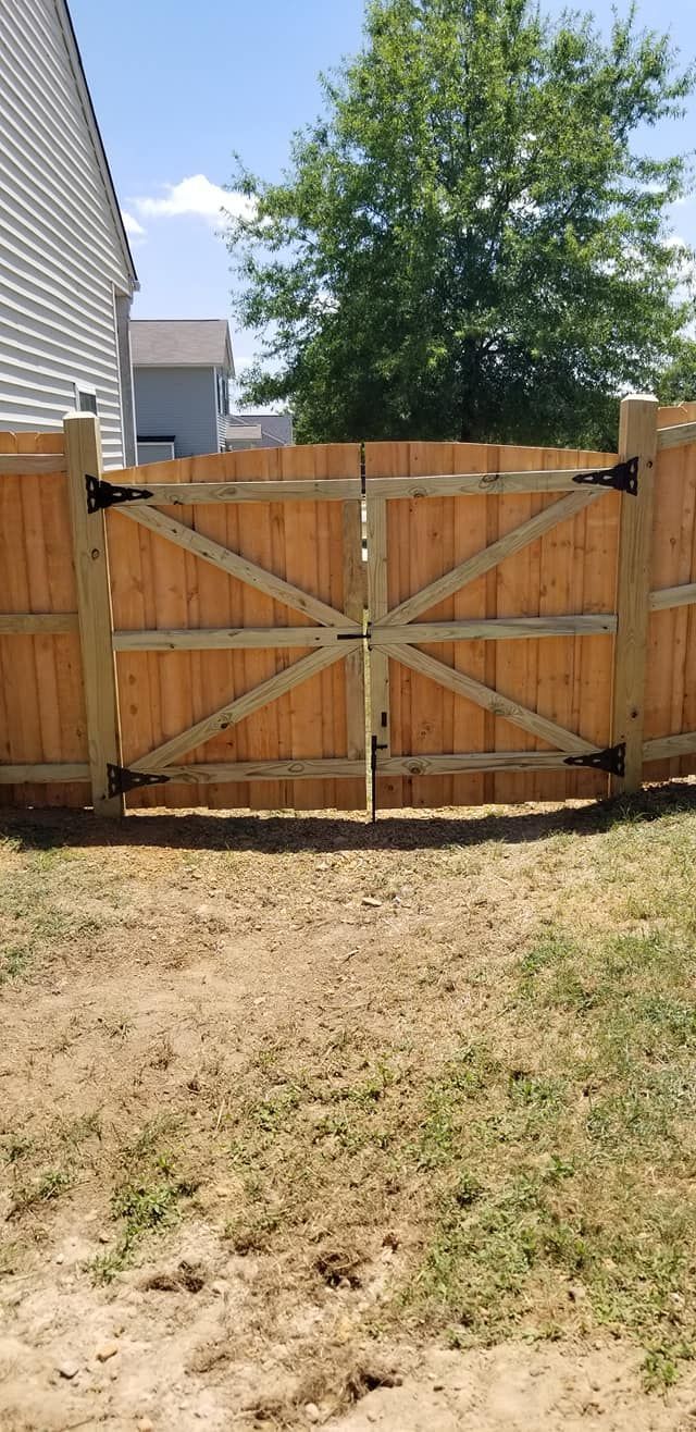 Wooden backyard gate in a fenced yard with grass and a tree behind it.