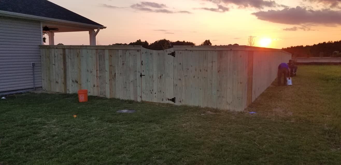 Backyard fence at sunset with a person near the right edge and an orange bucket by the house