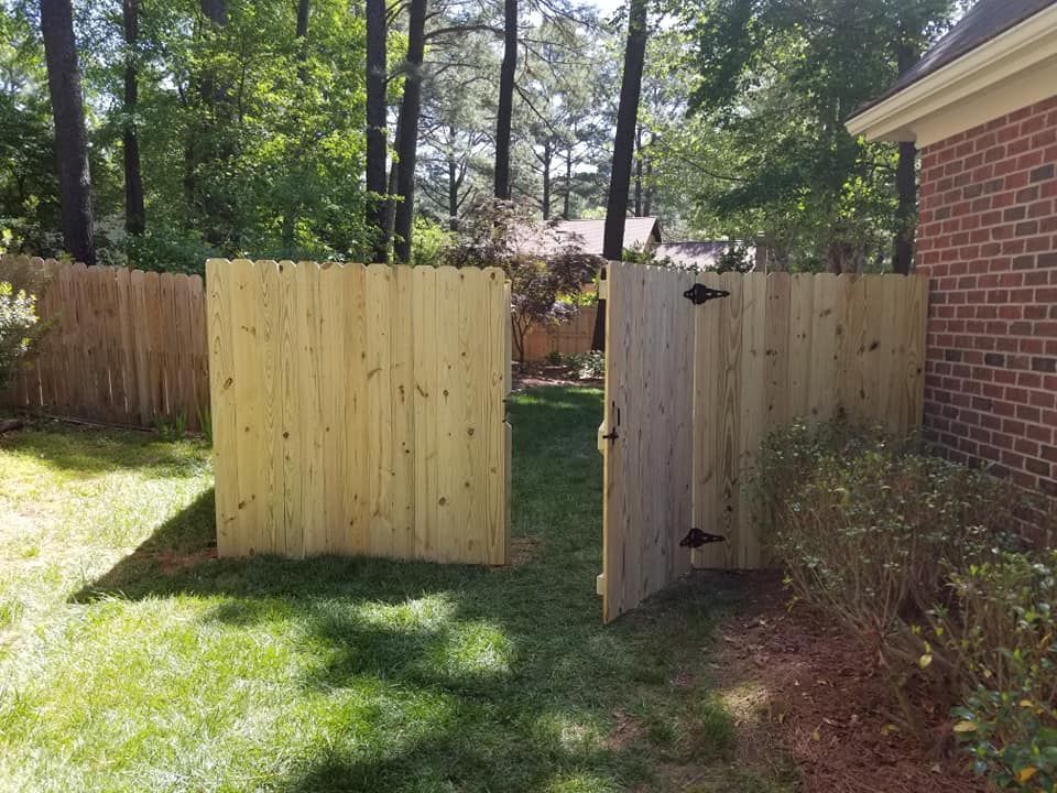 Open wooden gate in a backyard beside a brick house and fence