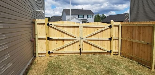 Wooden backyard fence with a central gate and side panels beside a house on grass.