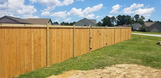 Wooden privacy fence along a grassy yard under a blue sky with clouds