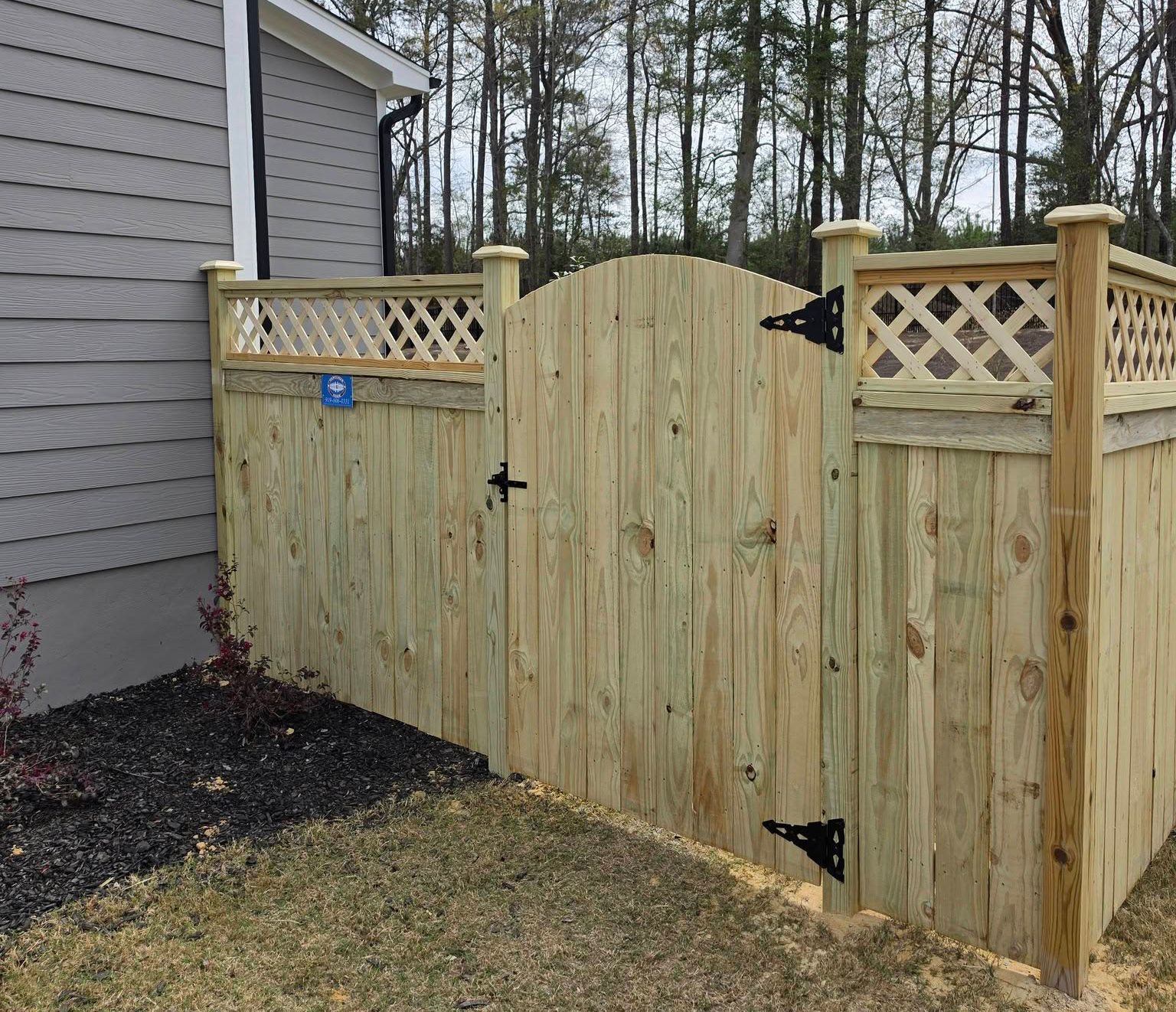 Wooden privacy fence with a closed gate beside a house and yard