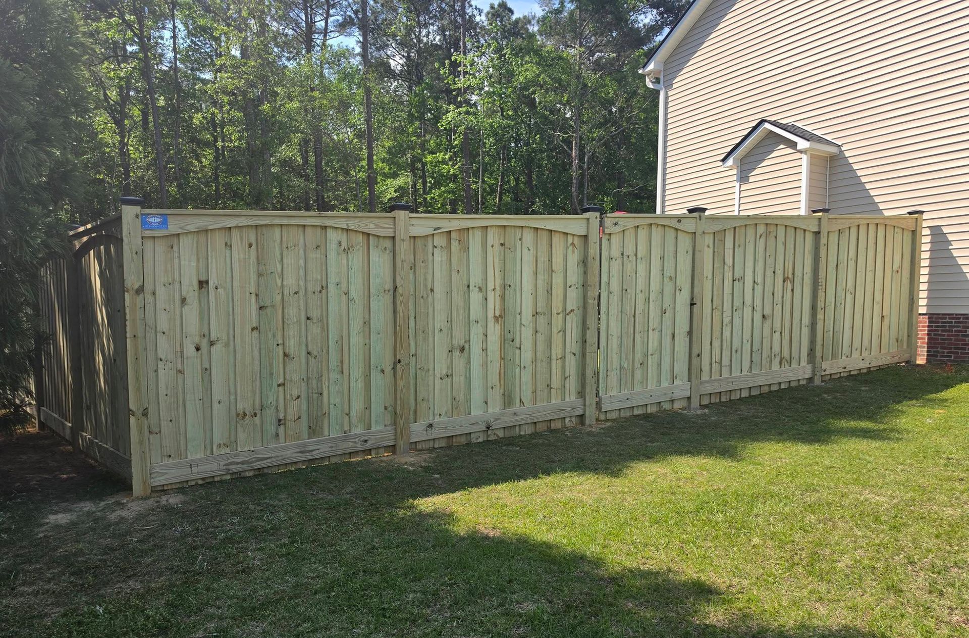 Wooden privacy fence along a house and grassy yard with trees in the background