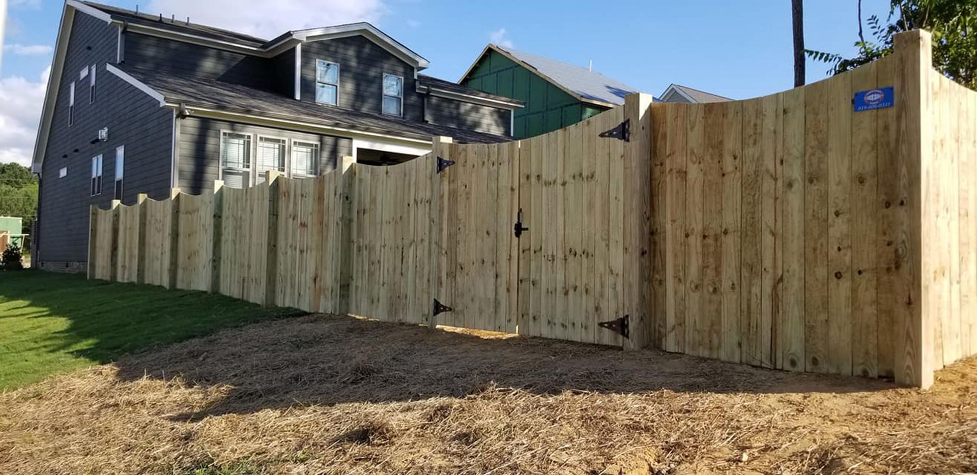 Wooden privacy fence along a grassy yard beside a gray house under a clear blue sky
