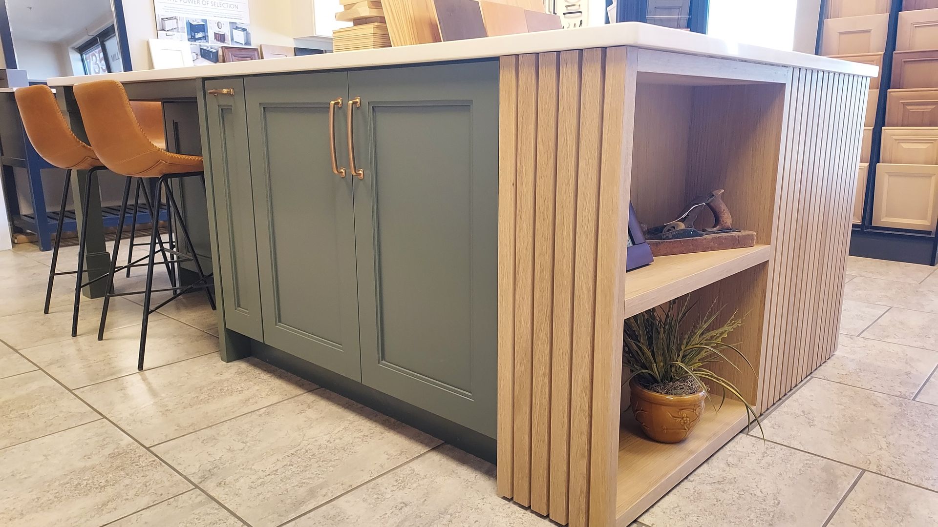 Kitchen island with green cabinets, butcher block sides, and a white countertop. Tan bar stools are to the side.