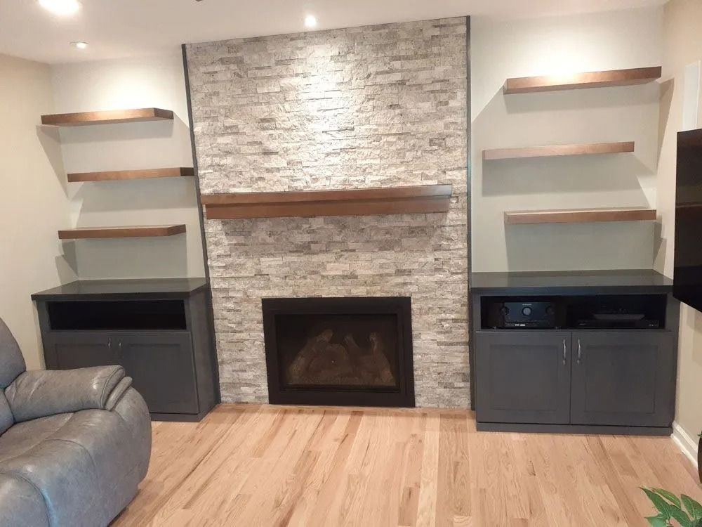 Living room with a fireplace, stone facade, gray cabinets, and floating wooden shelves.