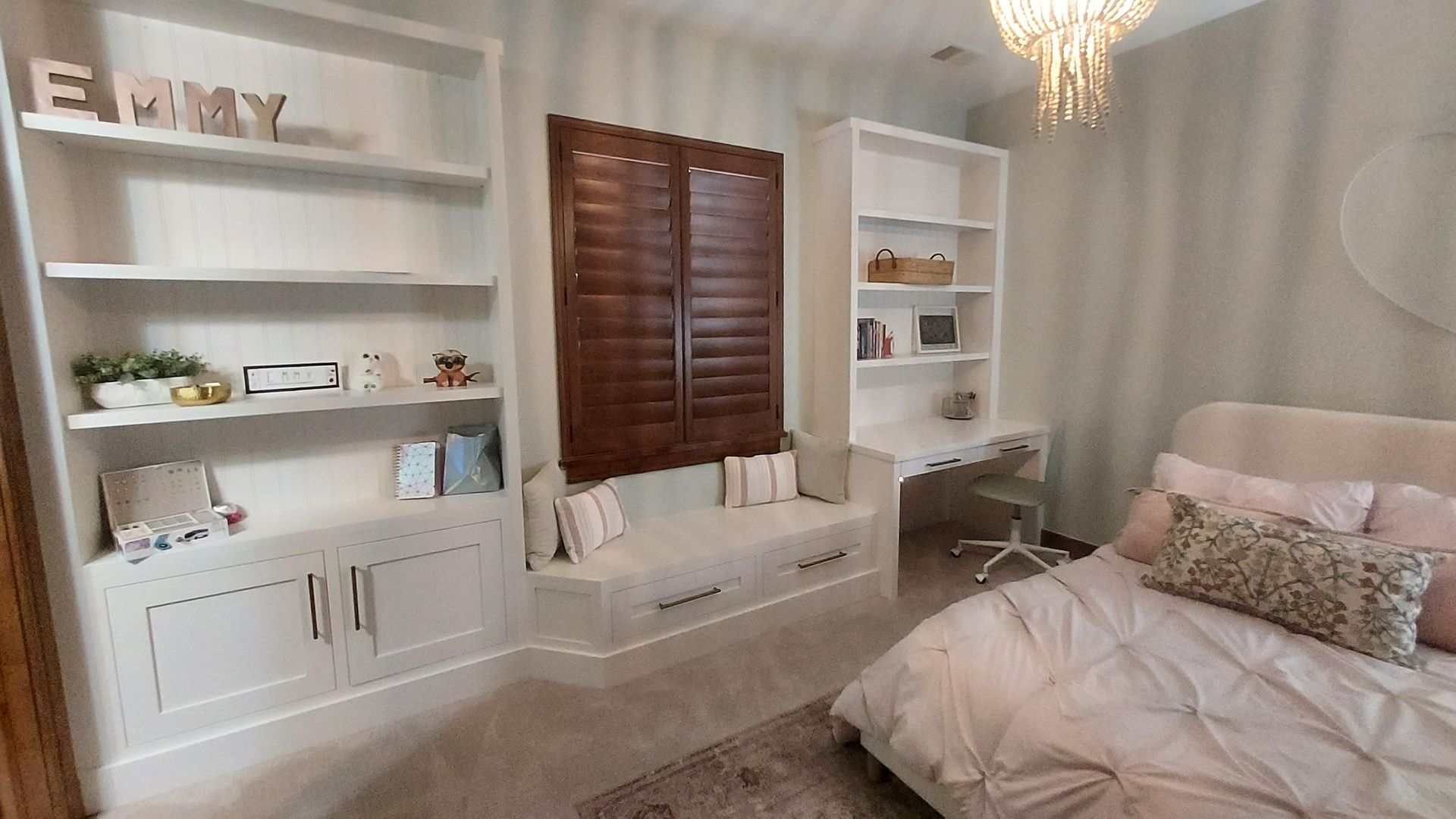 Girl's bedroom with built-in bookshelves, window seat, desk, and a bed with pink bedding.