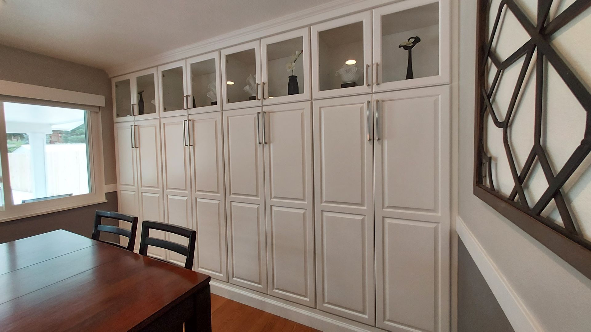 Dining room with built-in white cabinets, glass-front upper shelves, wood table, black chairs, and decorative wall art.