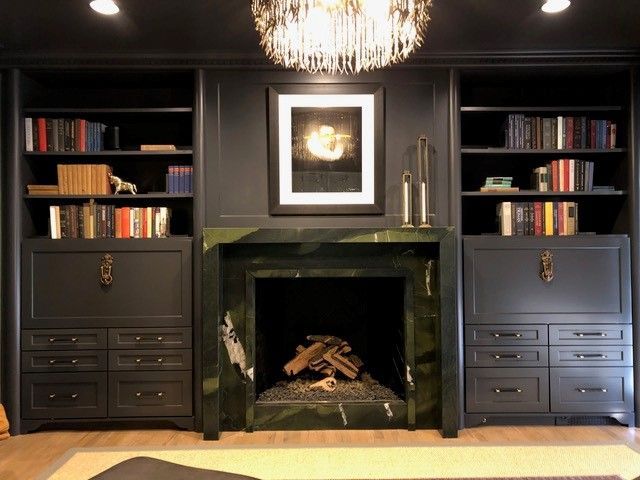 Built-in dark gray bookshelves flank a green marble fireplace with a decorative chandelier.