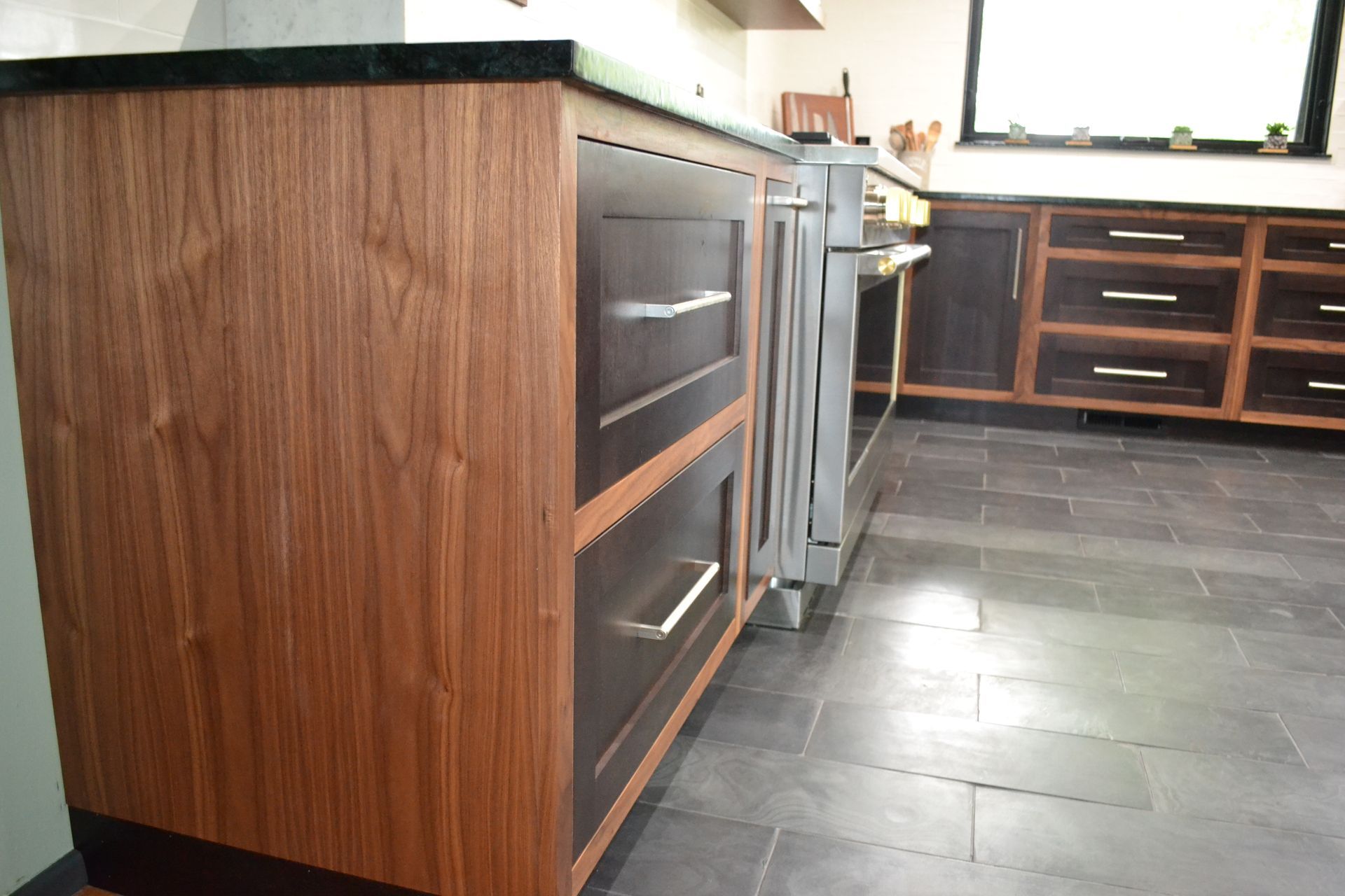 Kitchen cabinetry with dark wood and dark countertops, stainless steel appliances, and slate tile flooring.