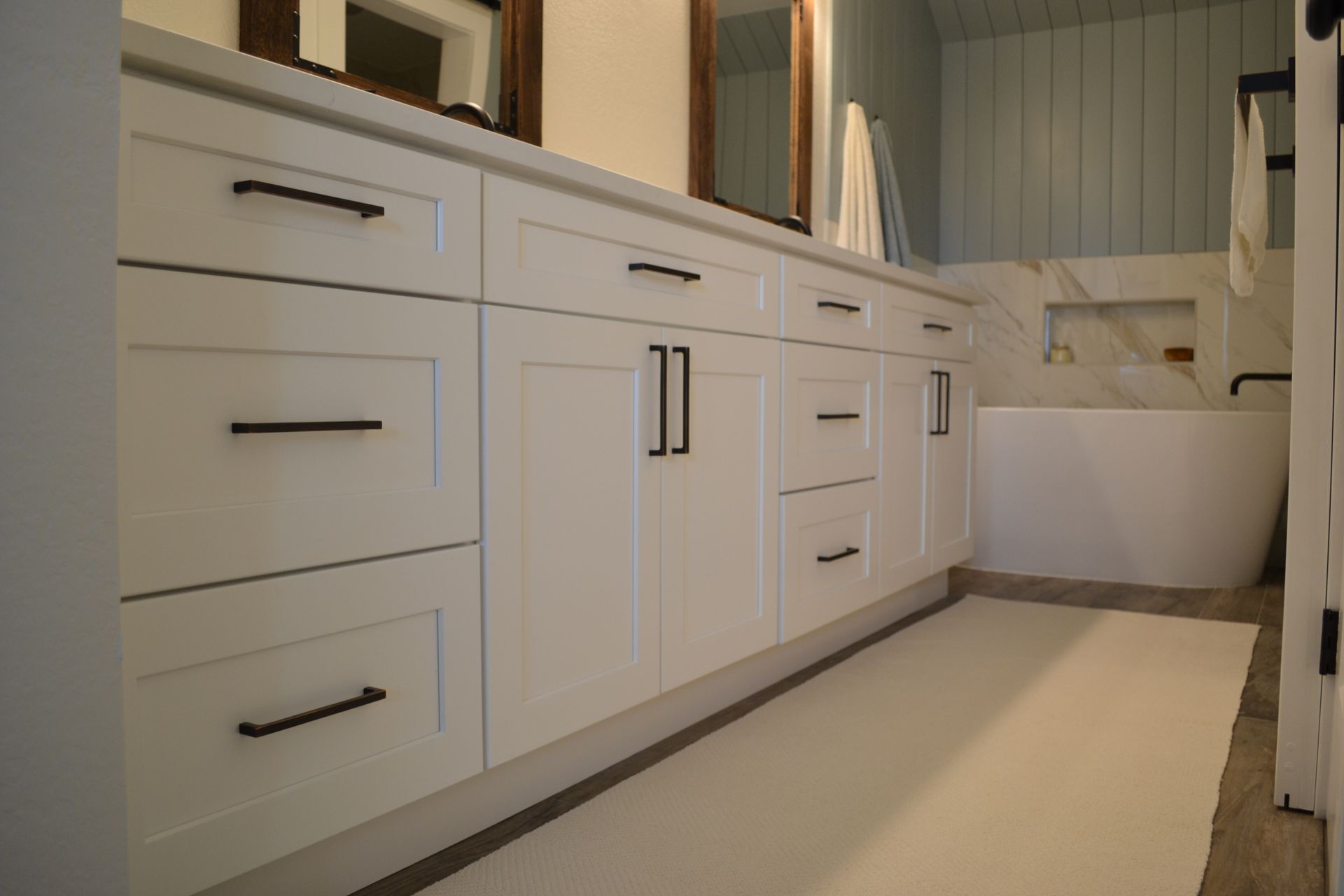 White bathroom vanity with black hardware, white countertop, and off-white rug.