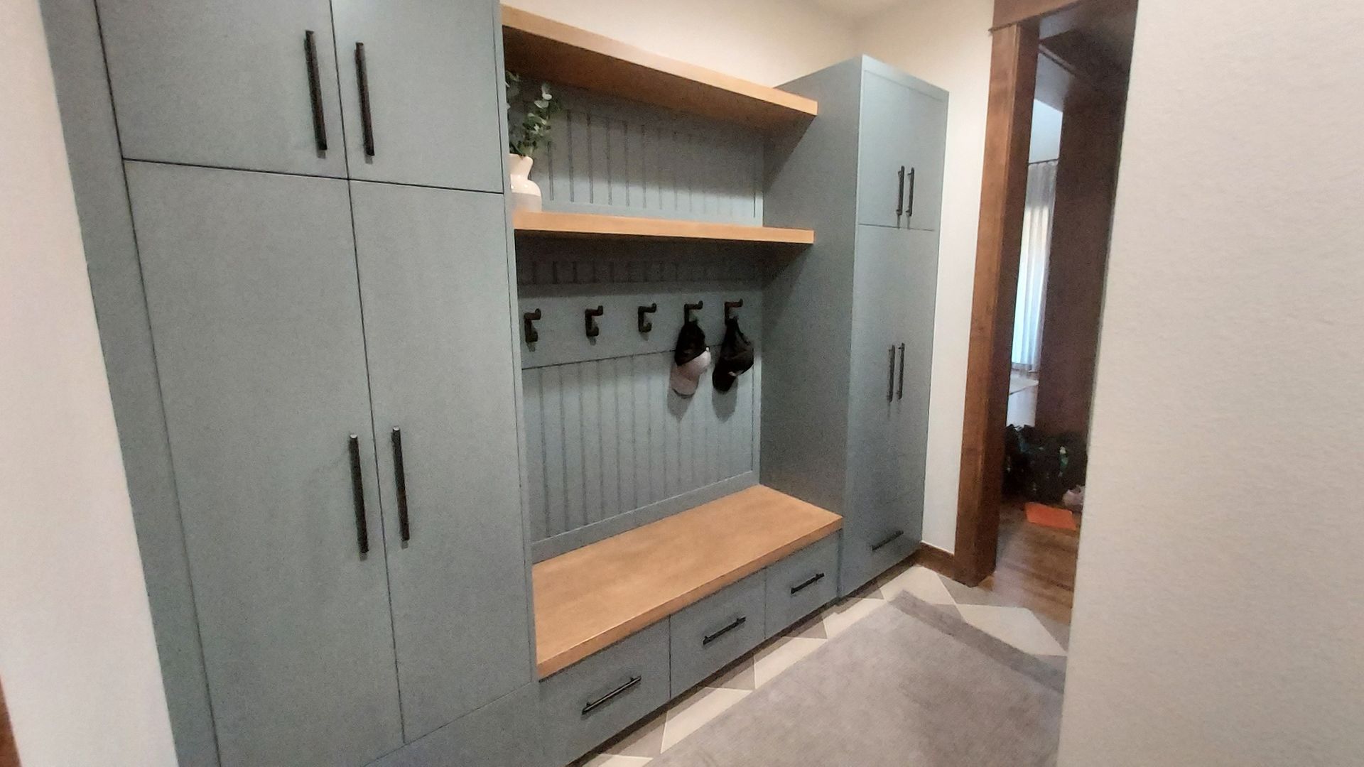 Gray and wood entryway with storage cabinets, bench, hooks, and shelving.