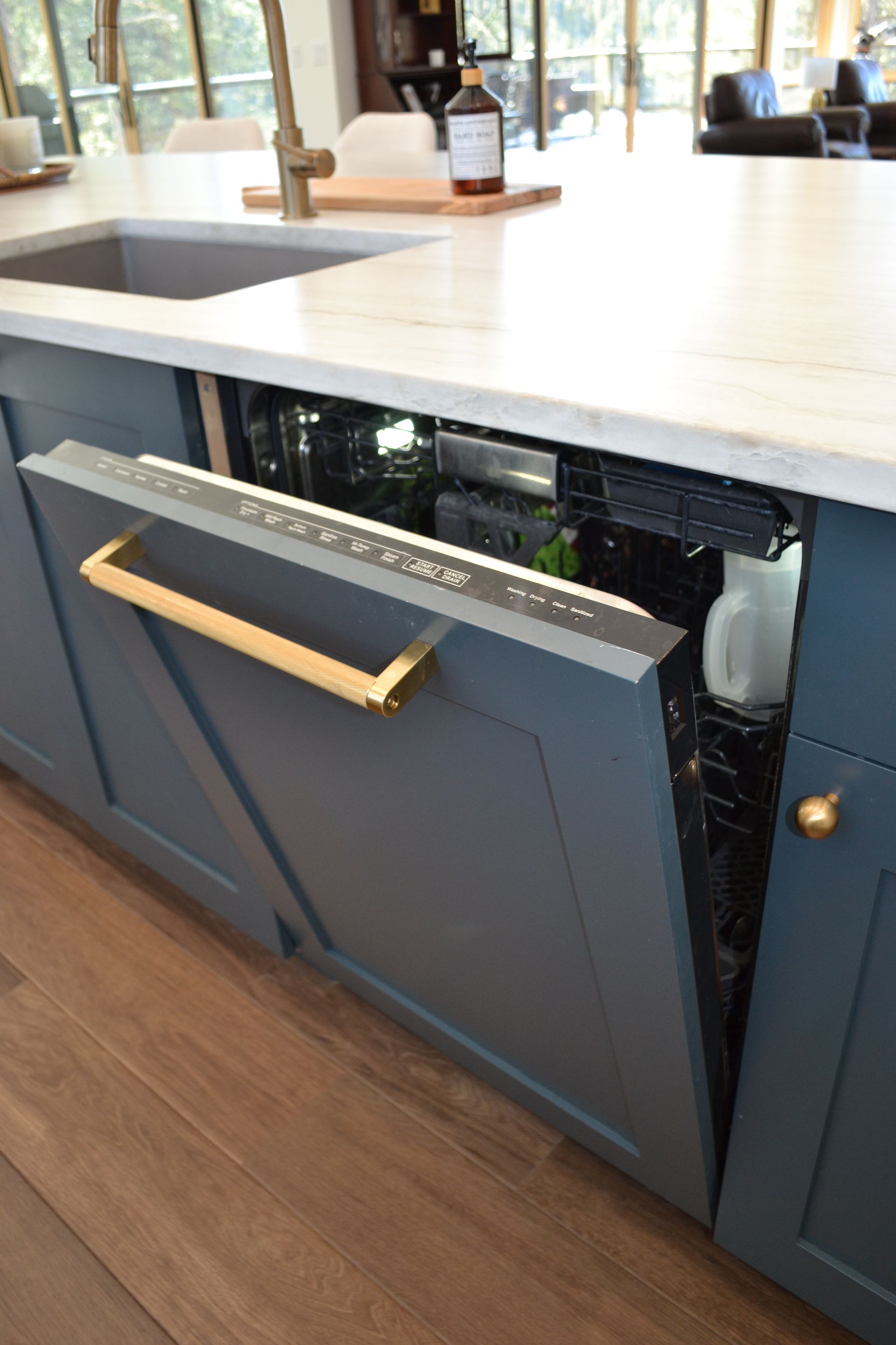 Opened dishwasher in a blue cabinet with a gold handle in a kitchen.