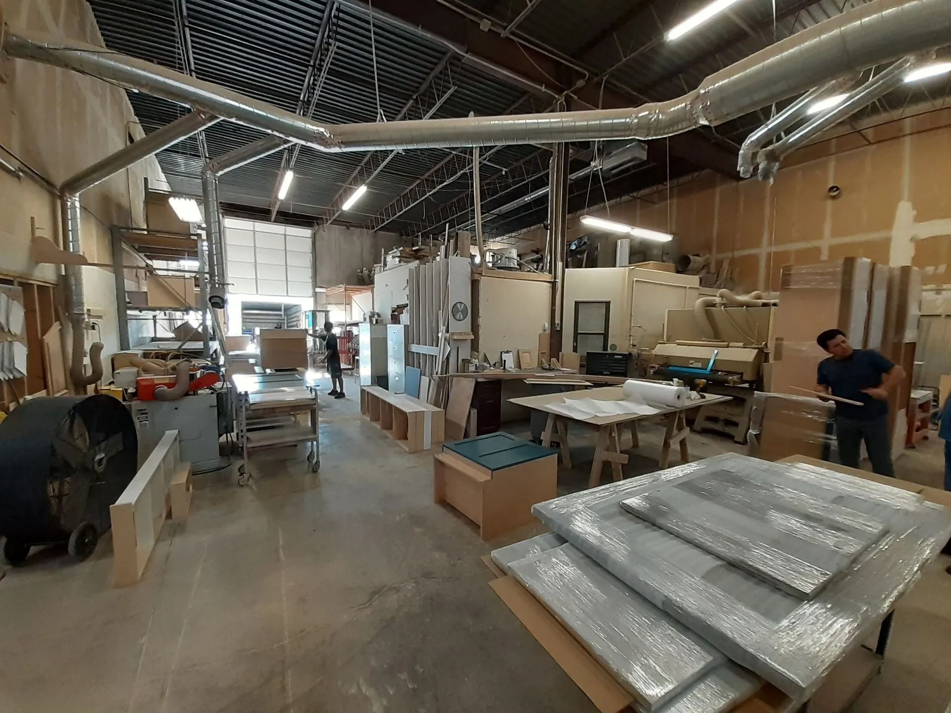 Interior of a woodworking shop with equipment, wood pieces, and workers.