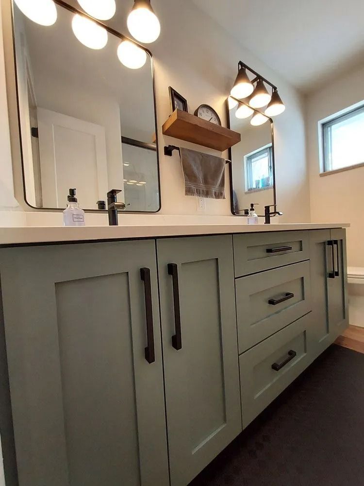 Sage green bathroom vanity with black hardware, mirrors, and lighting.