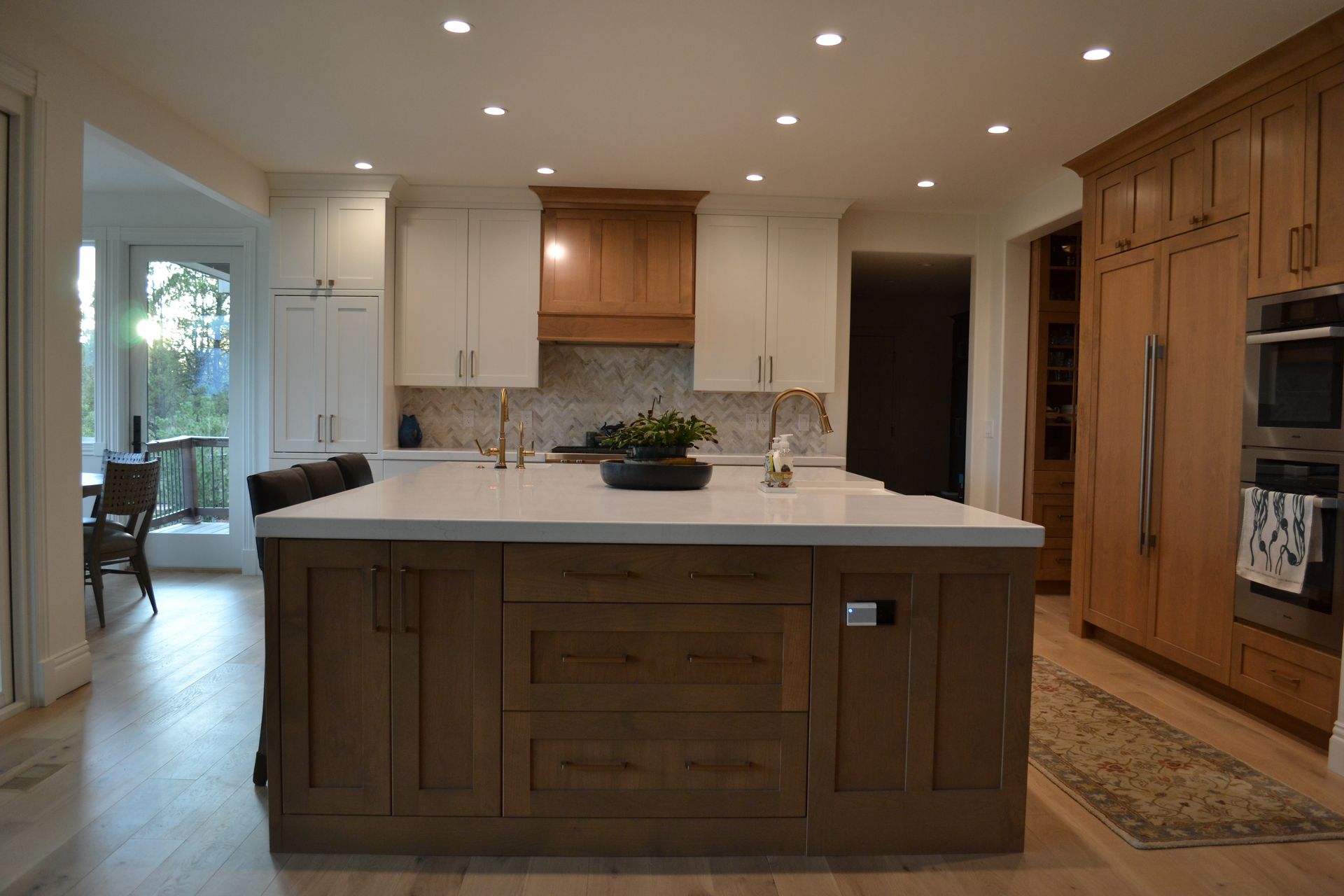 Kitchen with light wood floors, a dark wood island, white countertops, and white and wood cabinets.