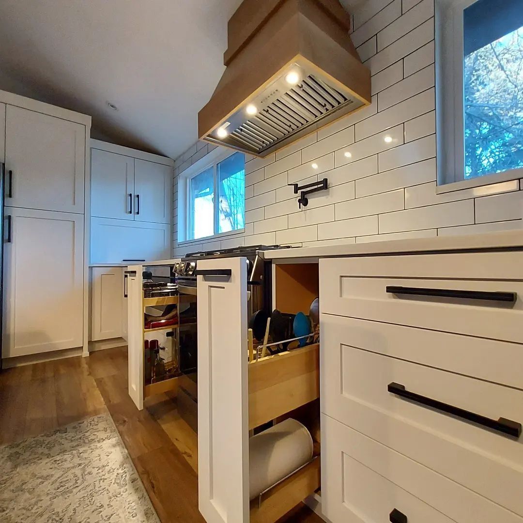 Modern kitchen with white cabinets, wood range hood, pull-out drawers, and natural light.