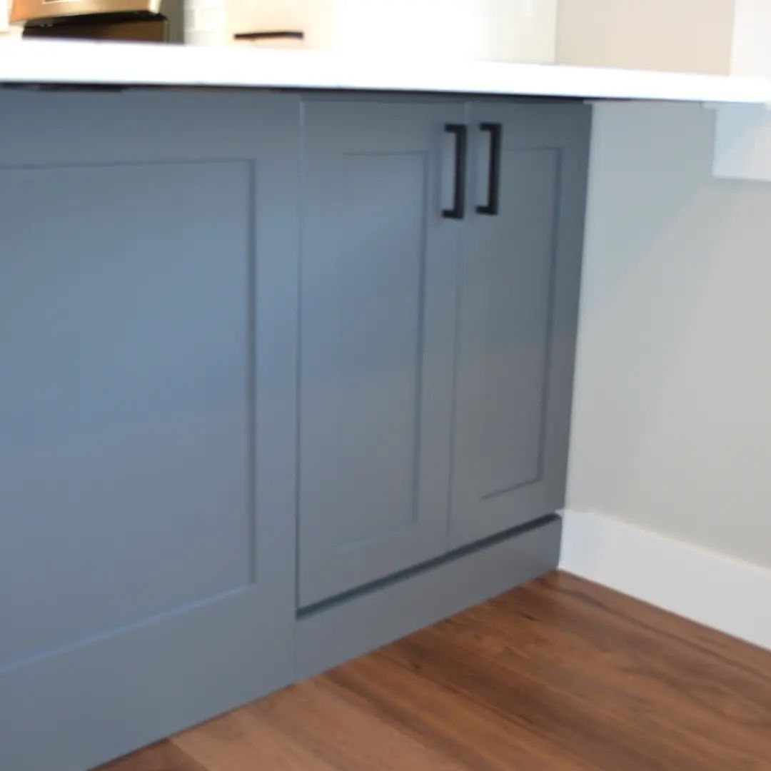Gray cabinet doors with black handles under a white countertop. Wooden floor.