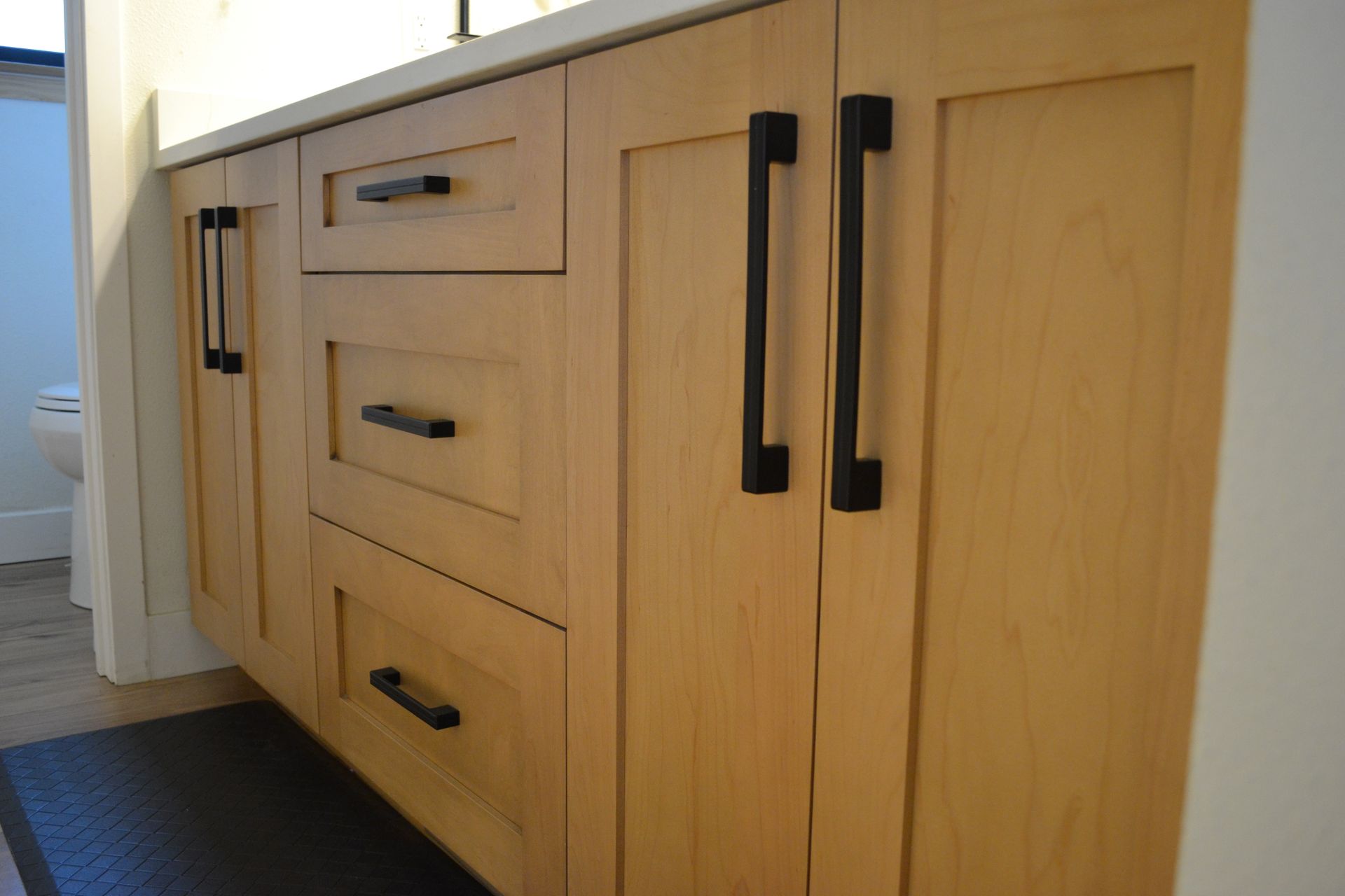 Wooden bathroom cabinet with black handles; drawers and doors visible.