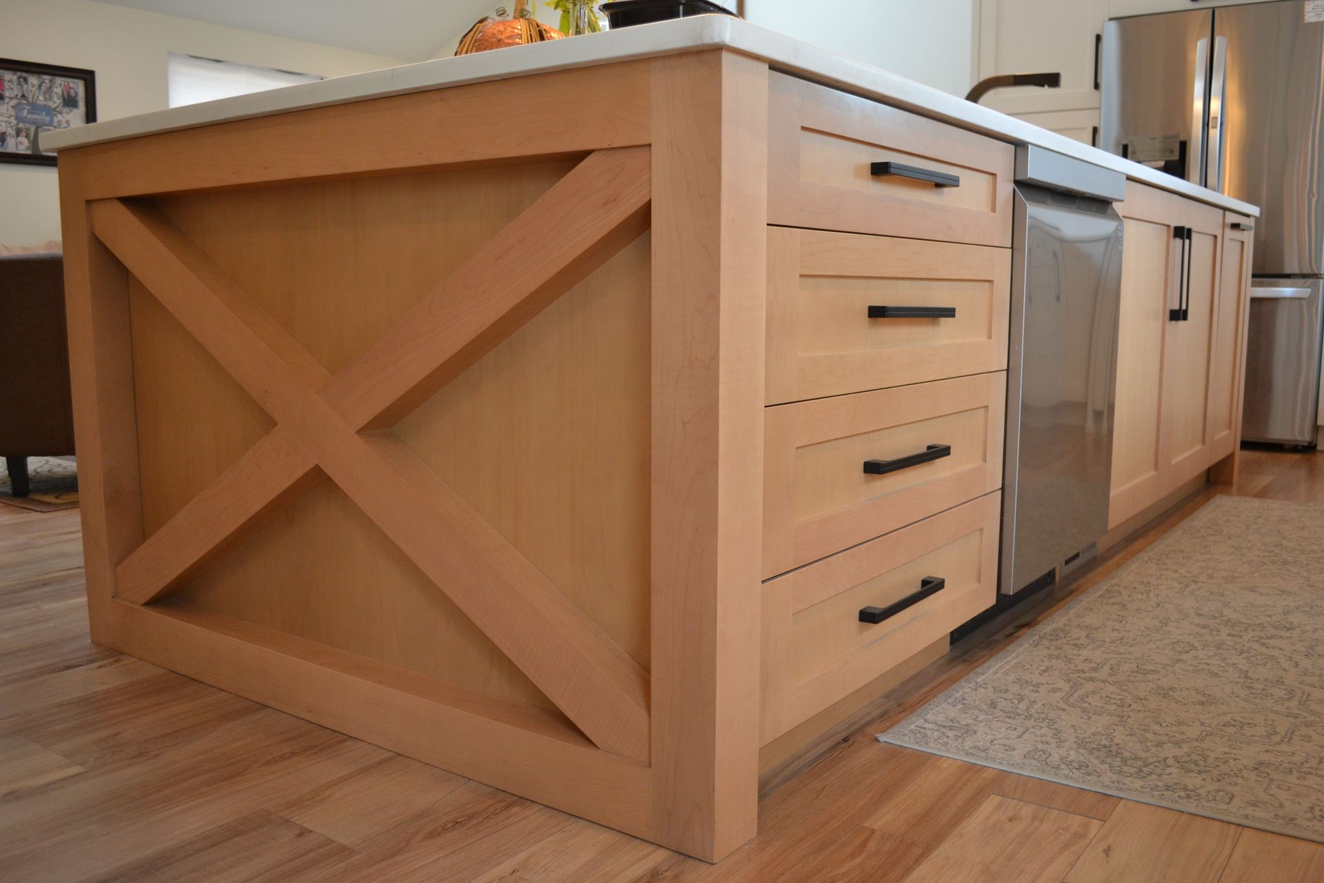 Kitchen island with light wood cabinetry, stainless steel dishwasher, and a white countertop.