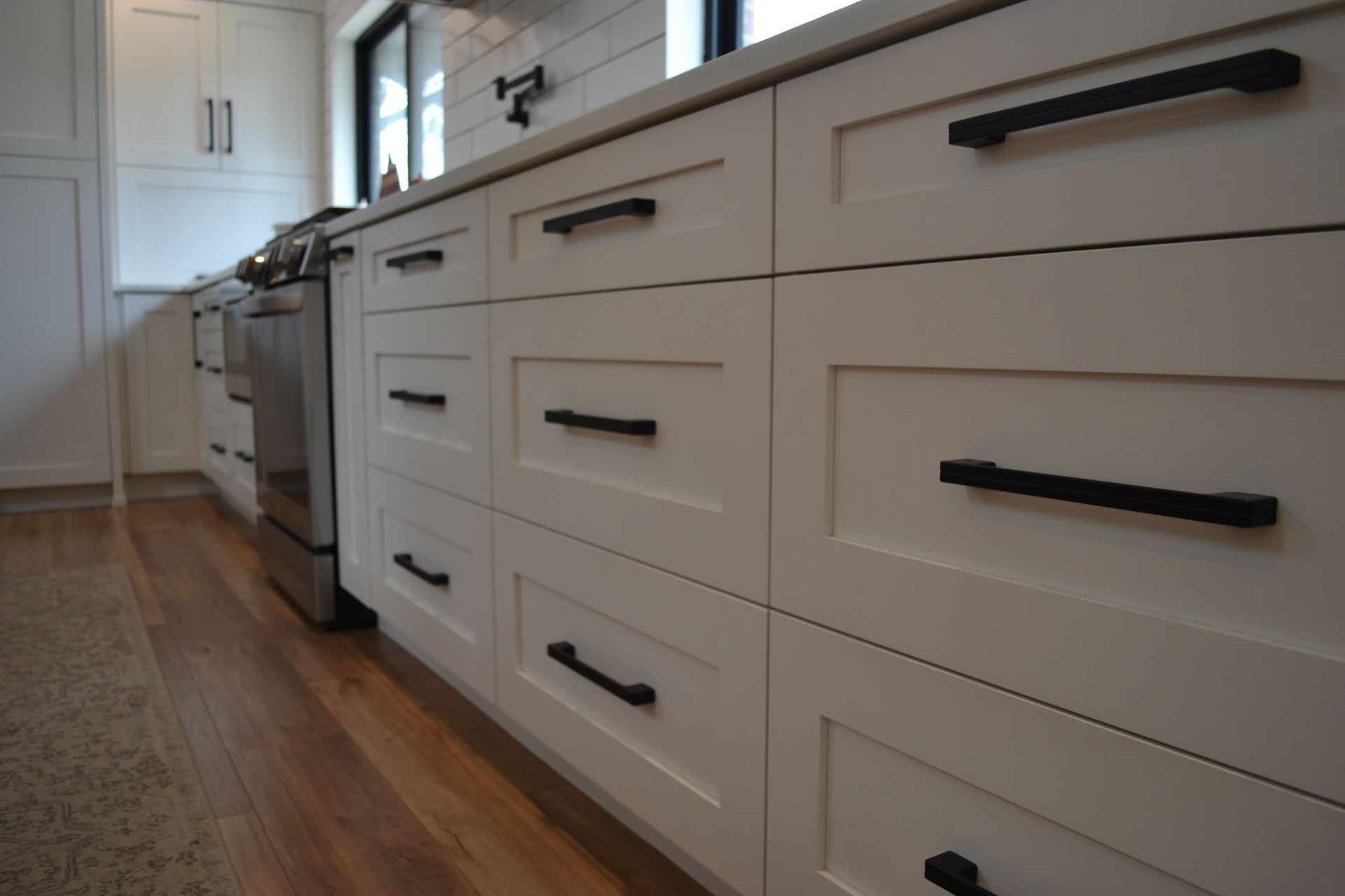White kitchen cabinets with black handles, set against wooden flooring.