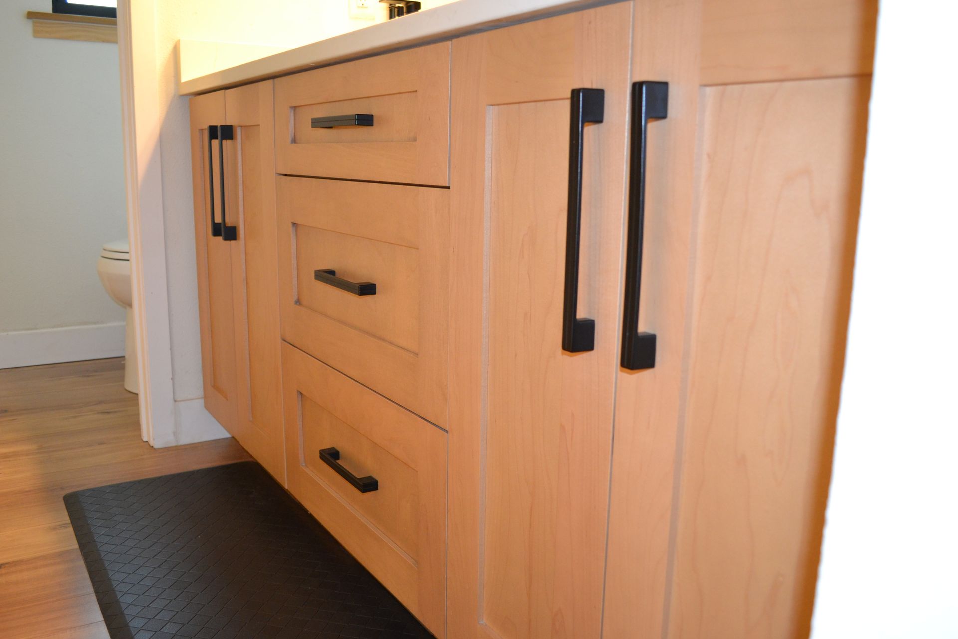 Light wood bathroom vanity with black handles.