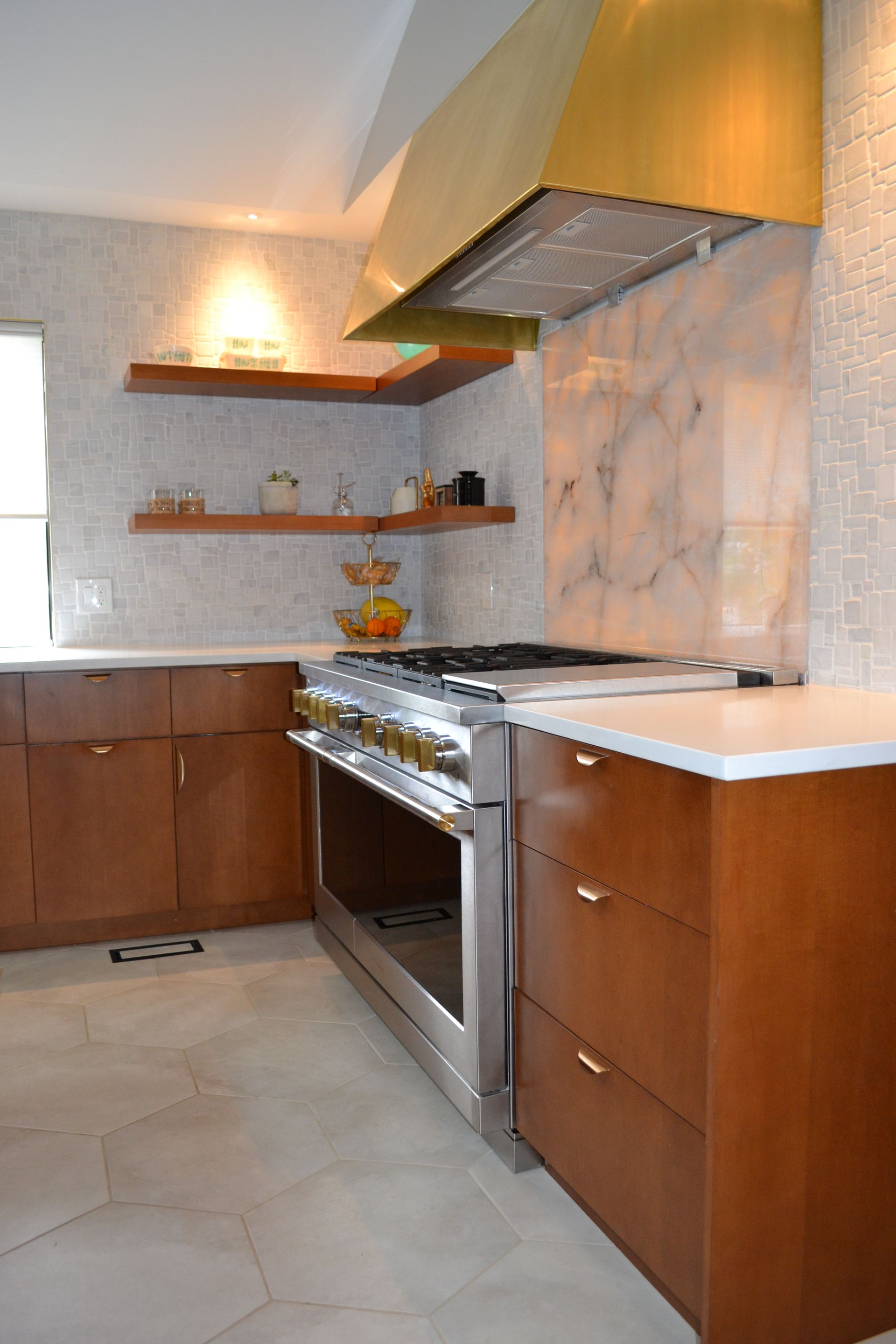 Kitchen with stainless steel range, brass hood, and wooden cabinets; white tile backsplash.
