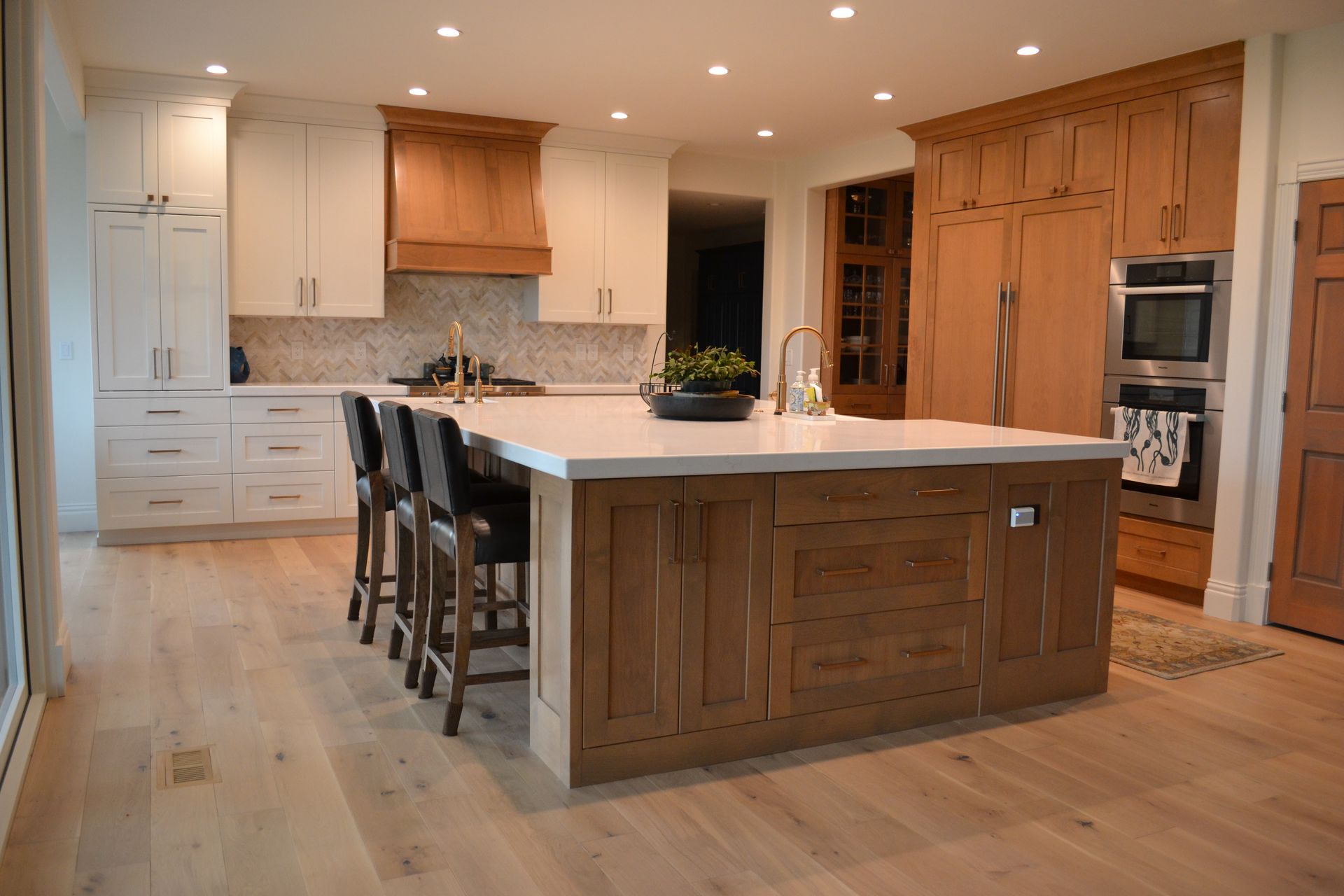 Kitchen with white and brown cabinets, island, stools, stainless steel appliances, and wooden floors.
