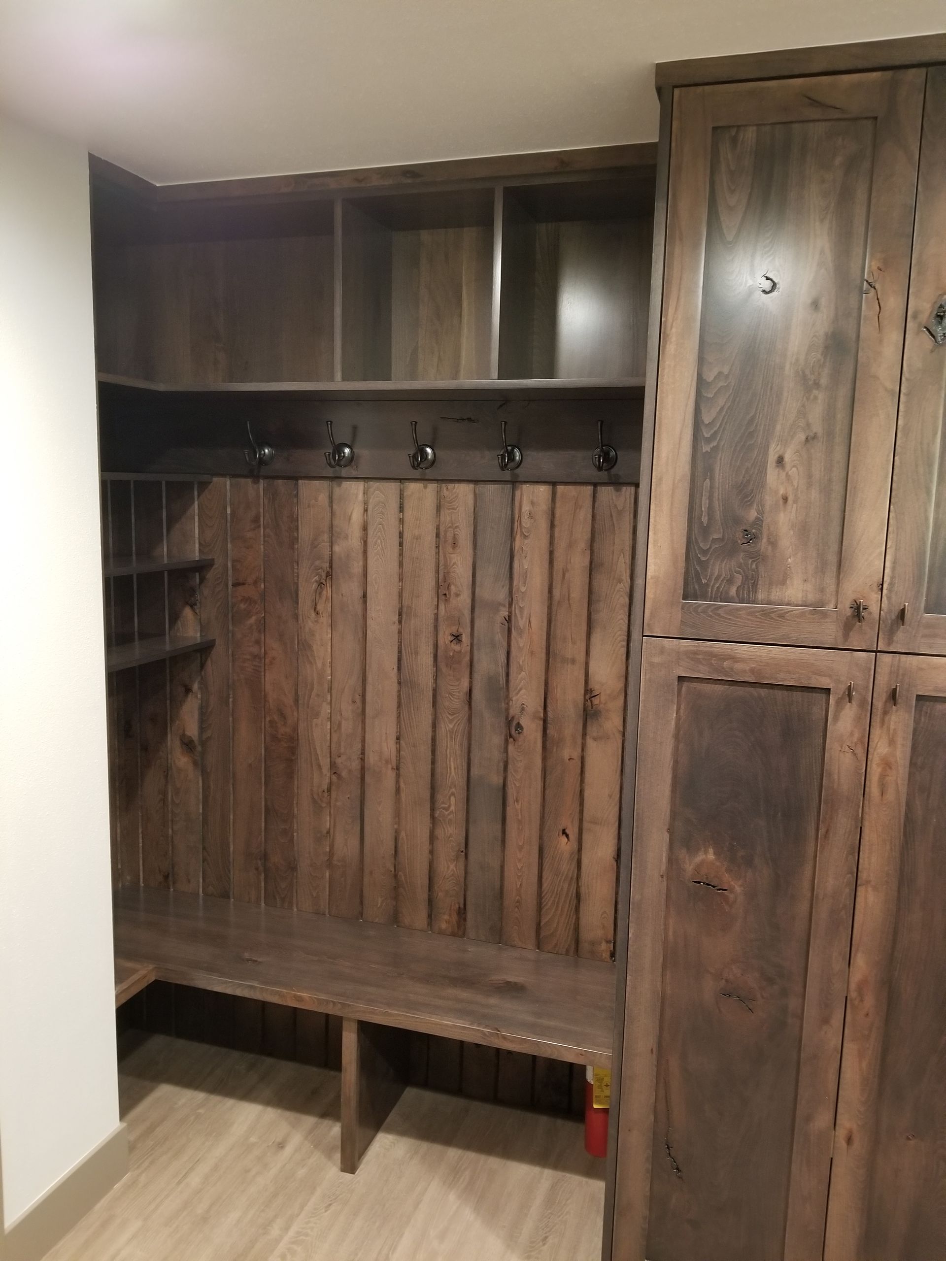 Wooden built-in mudroom with bench, hooks, and shelving.  Dark brown wood against light wood floor.