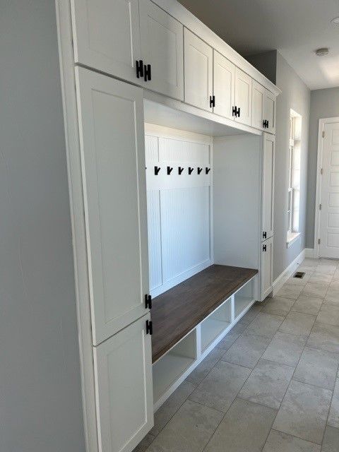 White built-in storage unit with hooks, bench, and upper cabinets in a hallway.