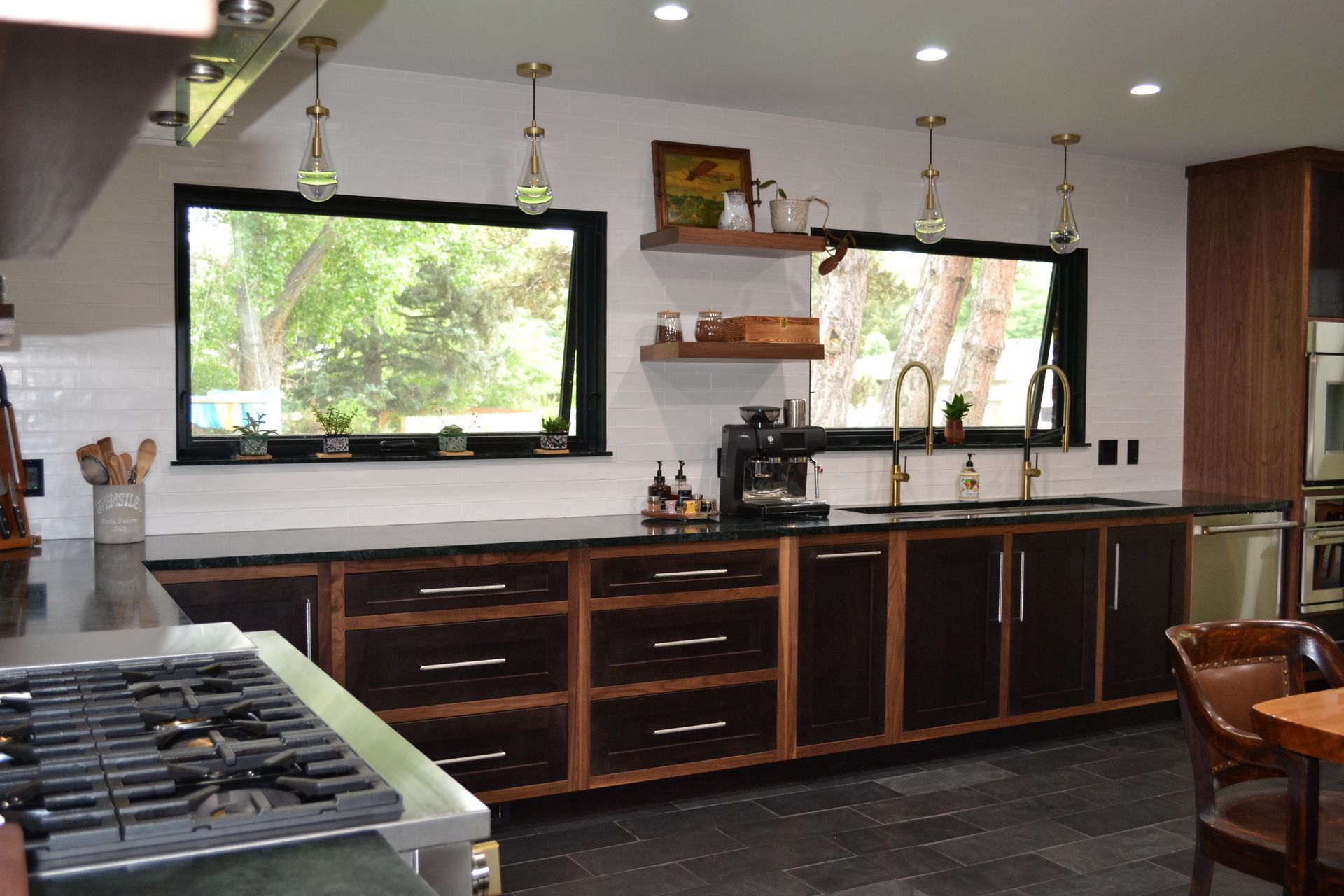 Modern kitchen with dark cabinetry, black countertops, and two windows.