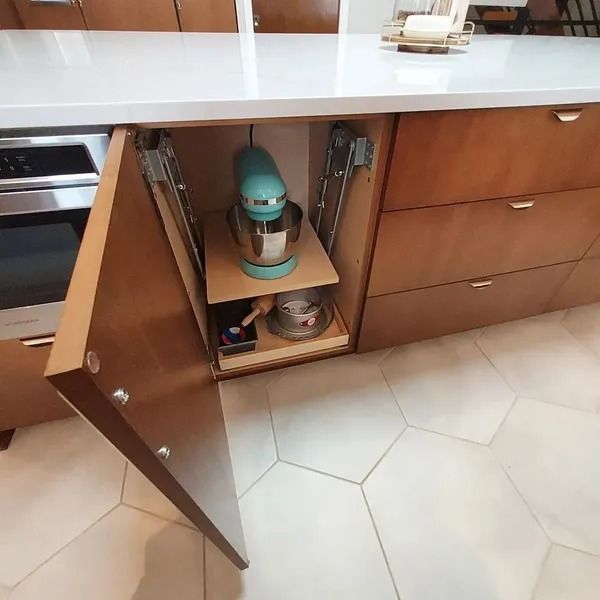 A pull-out kitchen cabinet with a teal stand mixer and accessories stored inside.