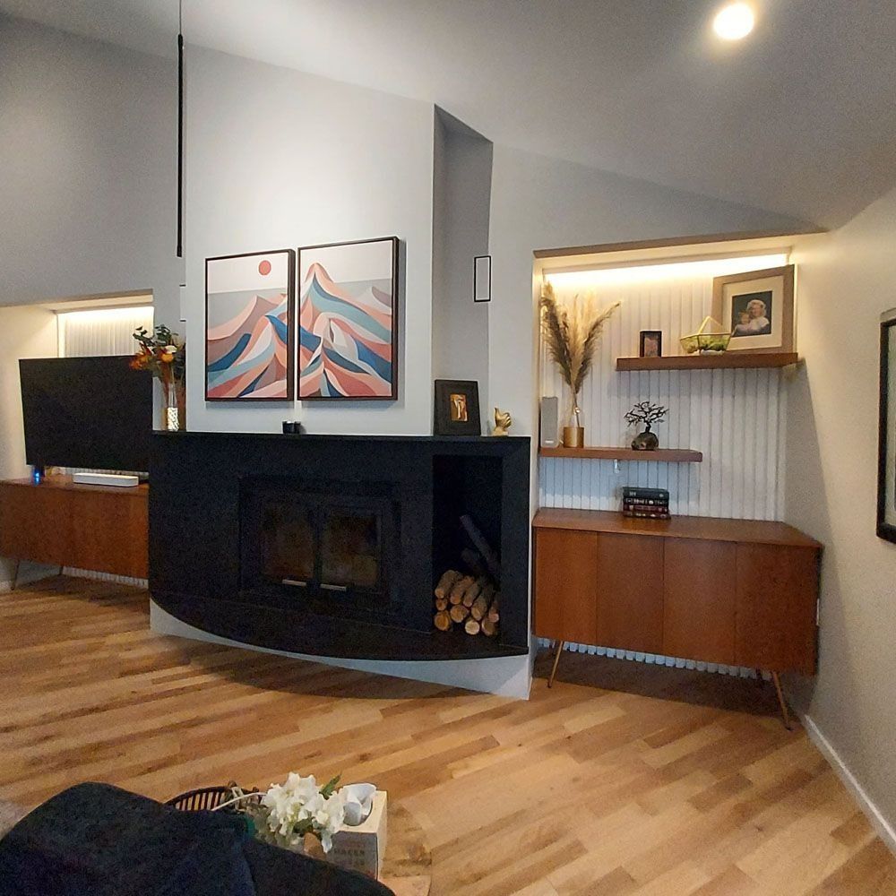 Living room with black fireplace, art, and wood cabinets. Light wood floor, white walls.