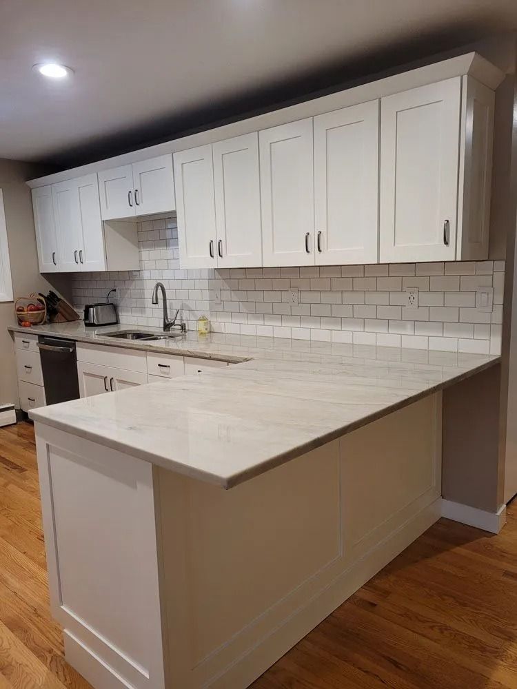 White kitchen with white cabinets, countertop and subway tile backsplash. Hardwood floor.