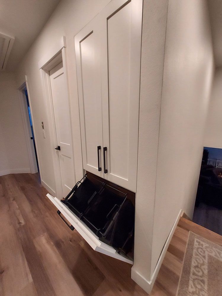 White storage cabinet with pull-out bins, in a hallway with wood flooring.