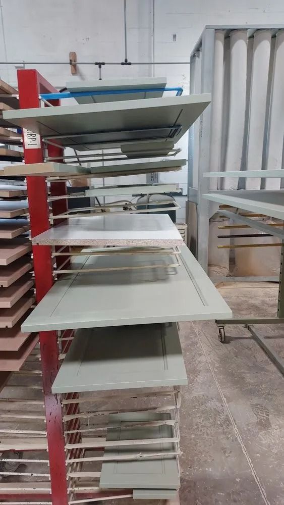 Shelves with freshly painted cabinet doors in a workshop, red support, green-gray color, indoors.