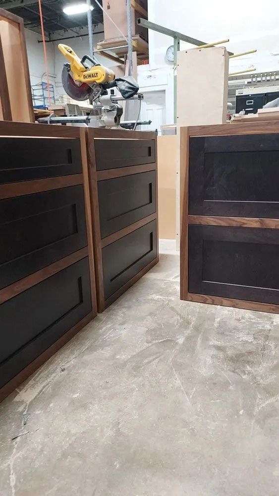 Three dark-stained wooden cabinets with brown trim, sitting on a concrete floor in a workshop.
