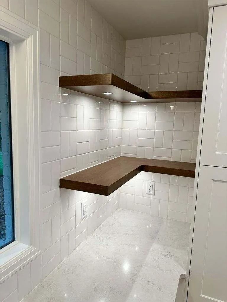 Corner pantry with white tiled walls, floating wooden shelves, and under-shelf lighting.