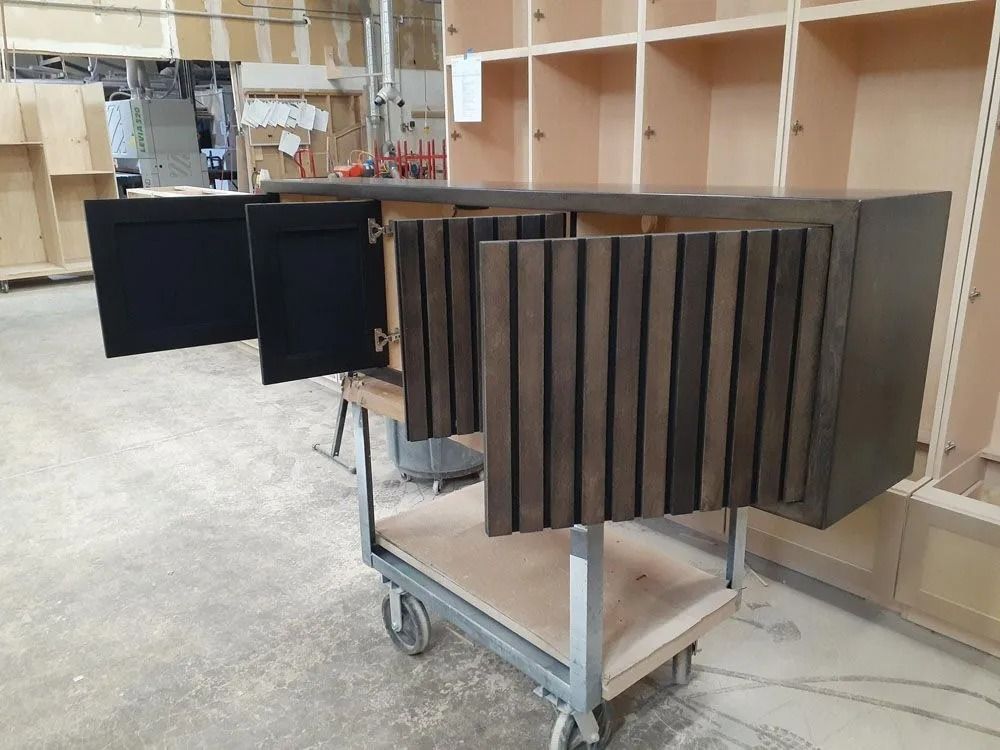 Dark wood cabinet with open doors, one with vertical slats, on a wheeled cart in a workshop.