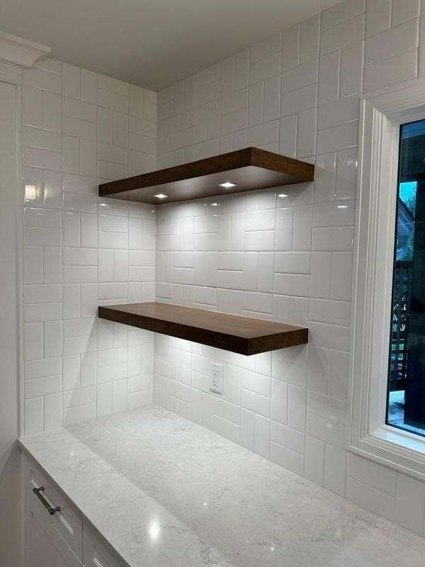 Two dark wooden shelves with built-in lights on a white tiled wall. A marble counter below.