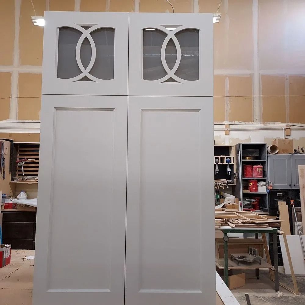 Tall white cabinet with decorative upper doors in a workshop setting.