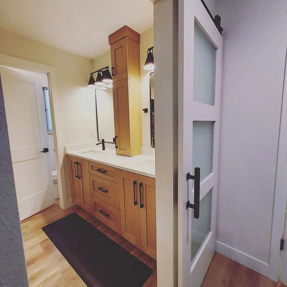 Bathroom interior: light wood cabinetry, white countertops, black hardware, frosted glass barn door.