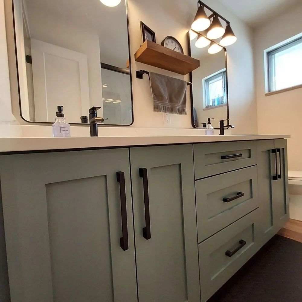Sage green bathroom vanity with black hardware, mirrors, and lighting fixtures.