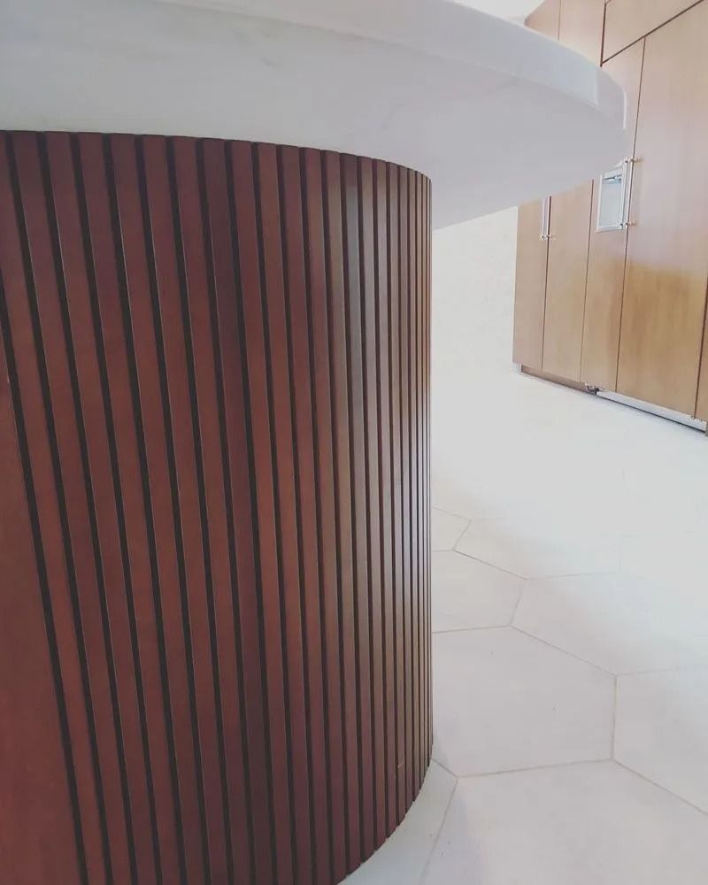 Dark wood-paneled cylindrical column supporting a white countertop. White tiled floor and light-colored wall are in background.