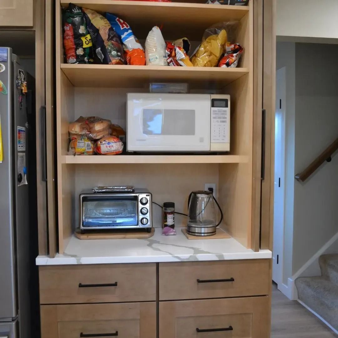 Kitchen cabinet with a microwave, toaster, and kettle on a countertop. Pantry items on shelves above.